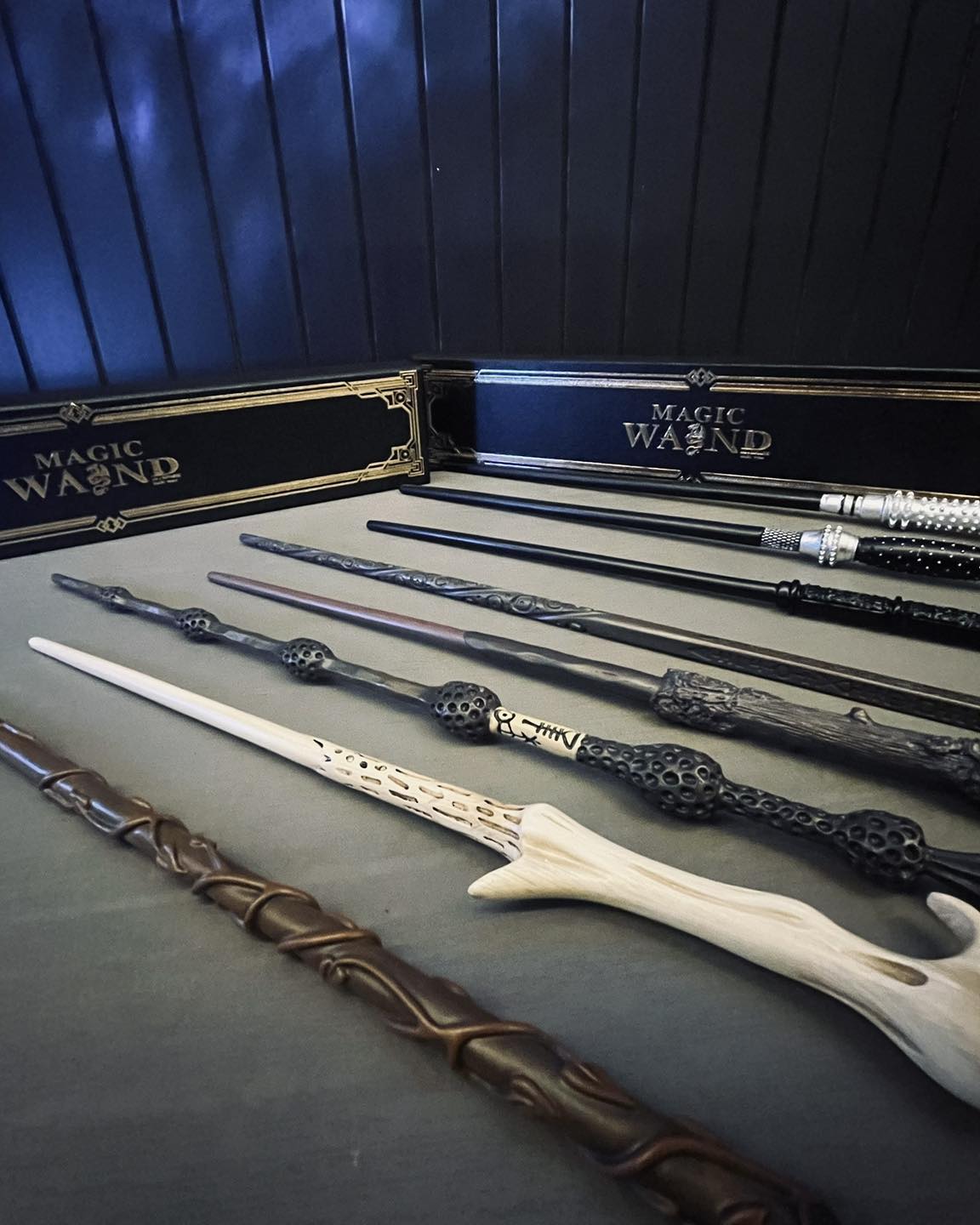 A collection of fantasy-style magic wands arranged on a dark surface, with two black boxes labeled 'MAGIC WAND' in the background.